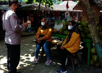 IMBAU PROKES–Personel Polsek Carita Polres Pandeglang, sedang mengimbau wisatawan yang berkunjung ke Pantai Carita, untuk menerapkan prokes, Minggu (26/9/2021). (NIPAL SUTIANA/SATELITNEWS.ID)