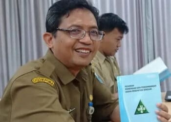 Sambil senyum sumringah, Sekretaris Dindikpora Pandeglang, Sutoto, menujukkan buku UKS yang sedang dipelajarinya. (ISTIMEWA)