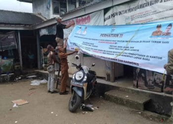 Anggota Satpol PP Kecamatan Menes, memasang spanduk sosialisasi relokasi PKL, Senin (16/1/2023). (ISTIMEWA)