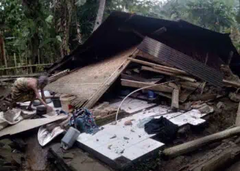 RUMAH ROBOH–Wanita paruh baya, sedang merapikan barang – barang berharga miliknya, pasca rumahnya roboh rata dengan tanah, Kamis (2/2/2023). (ISTIMEWA)