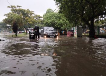 DORONG MOTOR: Salah satu ruas jalan di wilayah Kutabumi, Kecamatan Pasar Kemis, terendam banjir. Sejumlah pengendara sepeda motor terpaksa mendorong kendaraannya karena mogok akibat genangan air, Senin (12/1/2026). (ALFIAN/SATELIT NEWS)